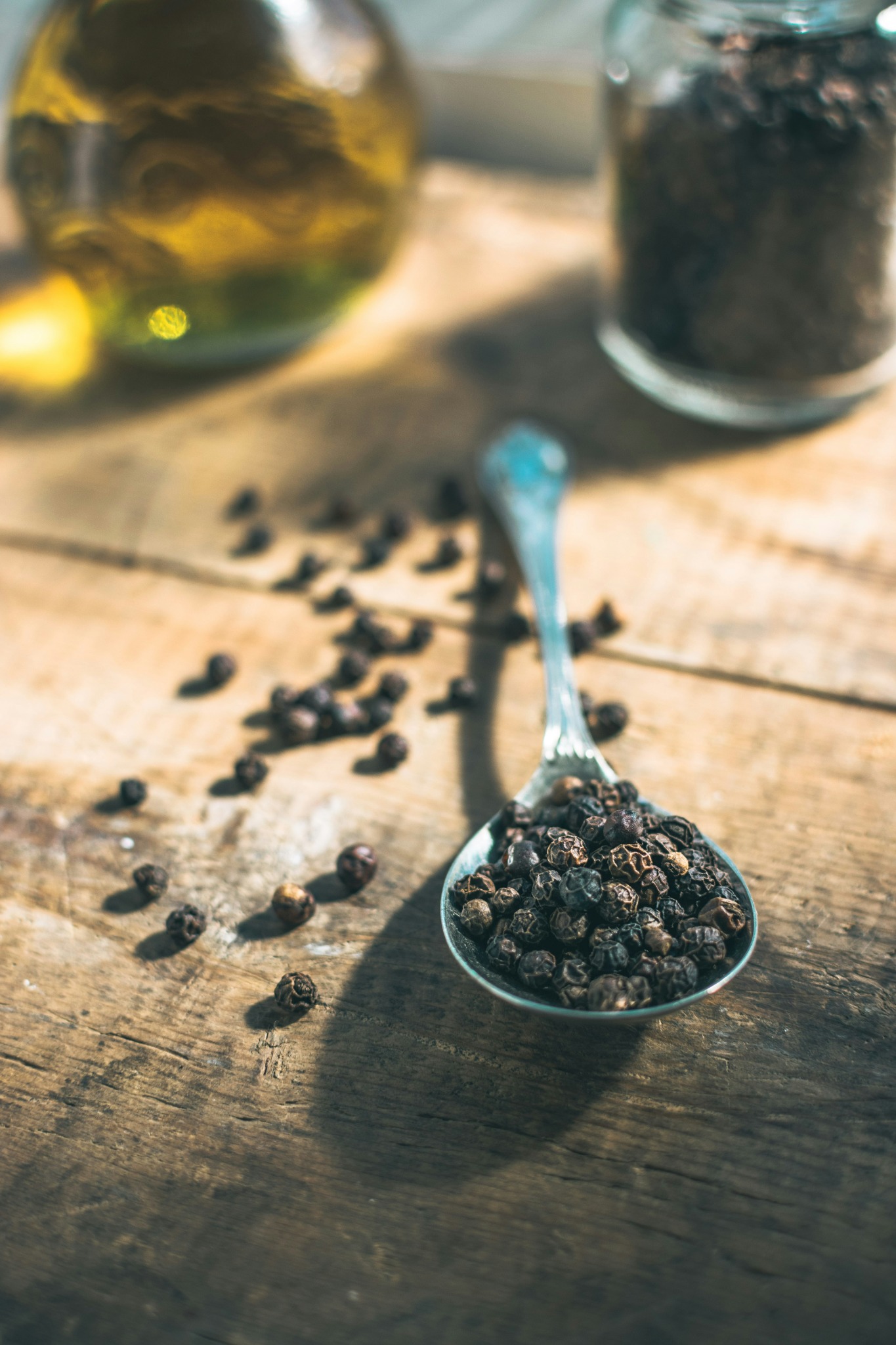 Peppercorns on a spoon beside olive oil